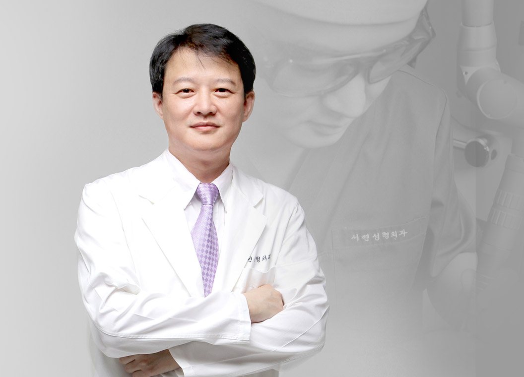 흰 가운 차림으로 팔짱을 낀 서연성형외과 김민규 대표원장(뒤로 흐릿한 수술 장면)